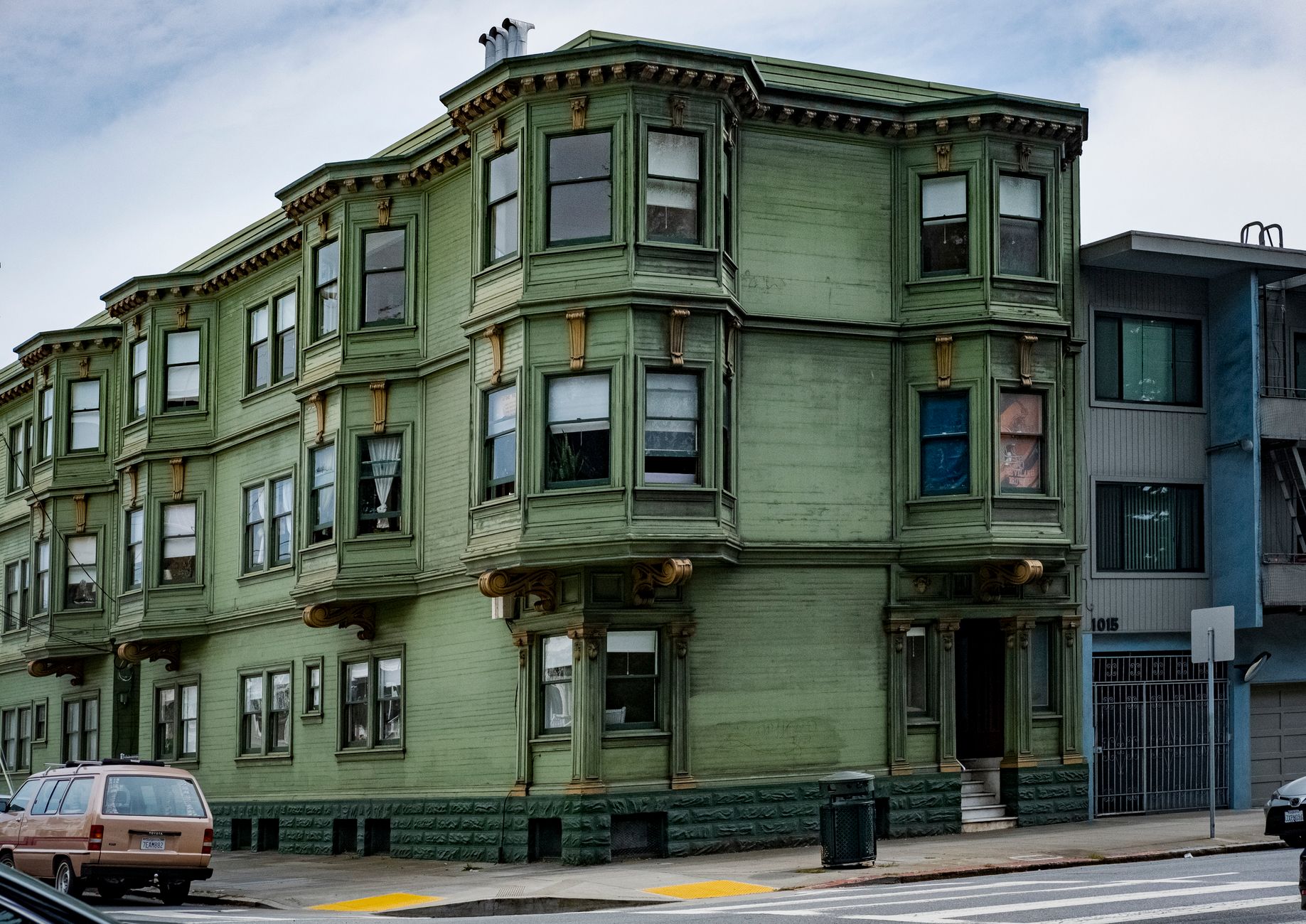 A vibrant green Victorian apartment building on a street corner with classic architectural details.