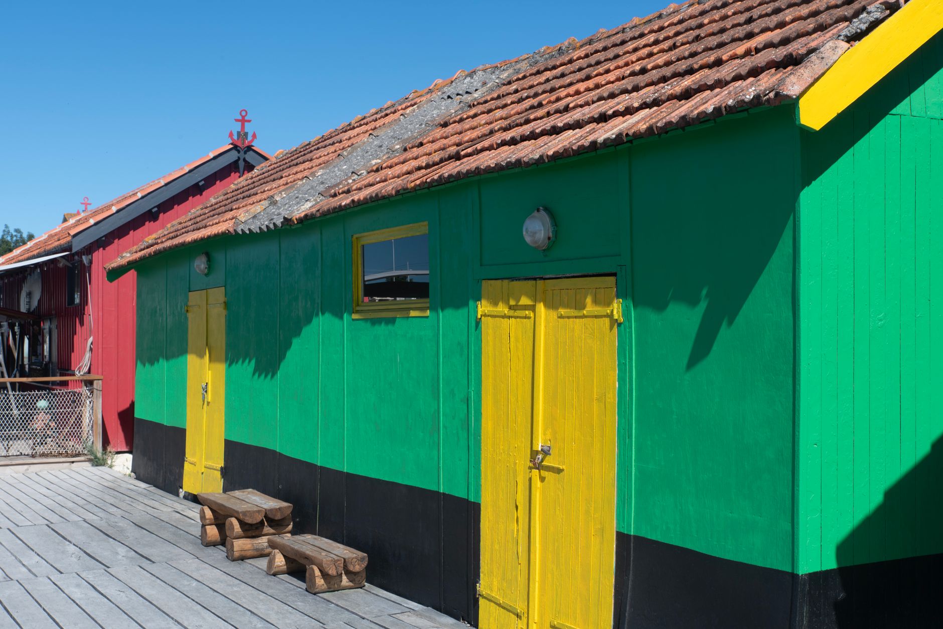 Vivid beach huts with yellow doors and green and red walls under a clear blue sky.