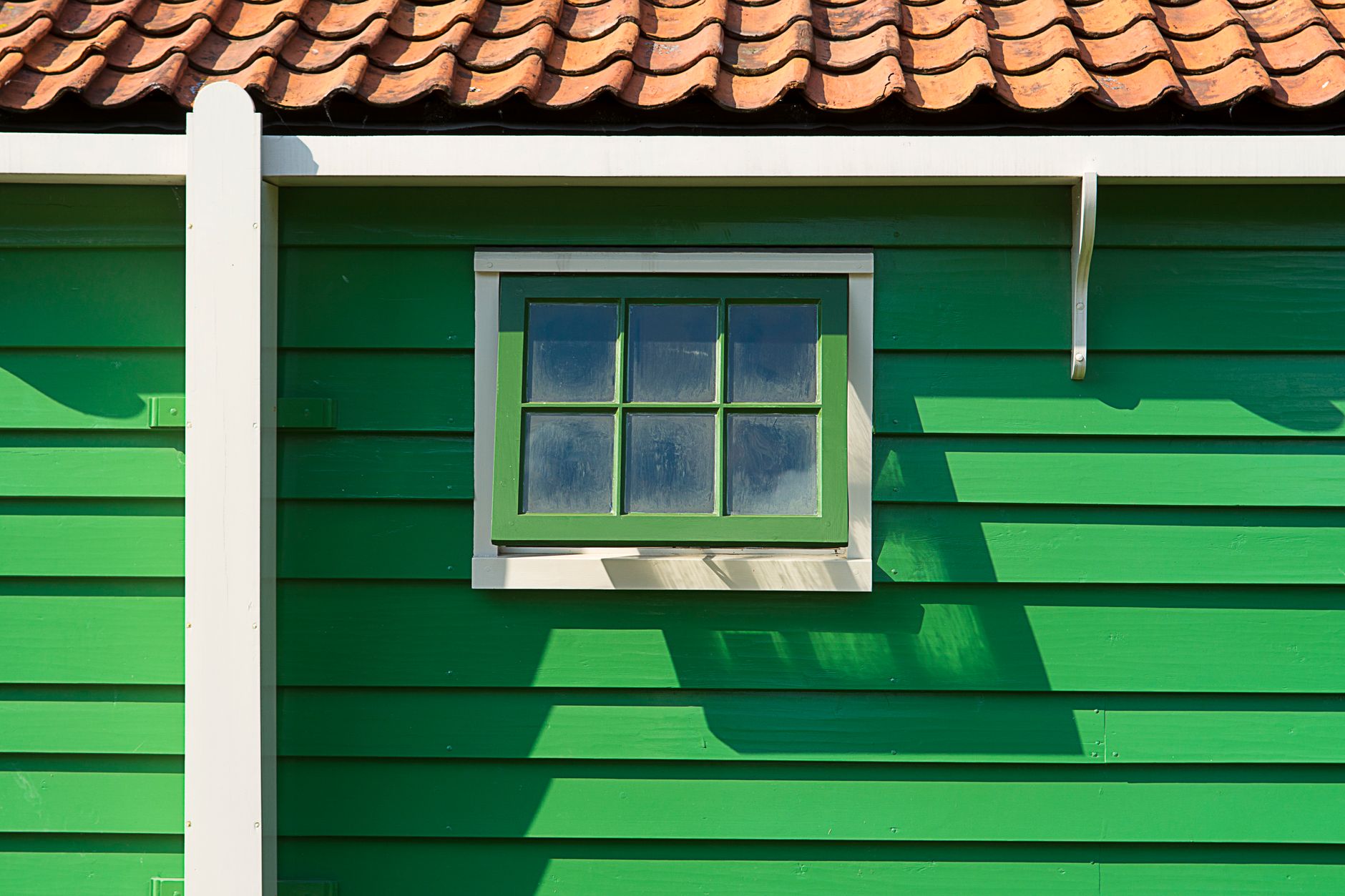 Close-up of a vibrant green wooden house with a small window and terracotta tile roof.