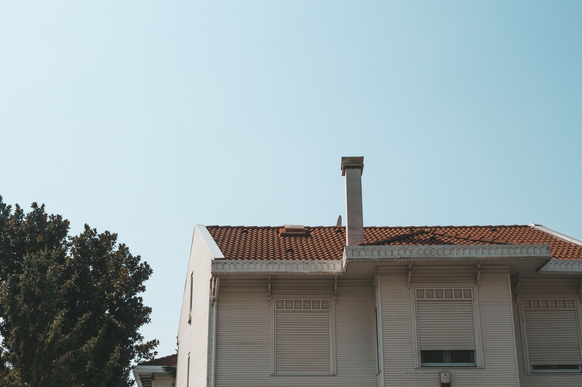 Facade of cozy residential house with white walls and shutters of minimalism style on windows located in sunny countryside on clear summer day
