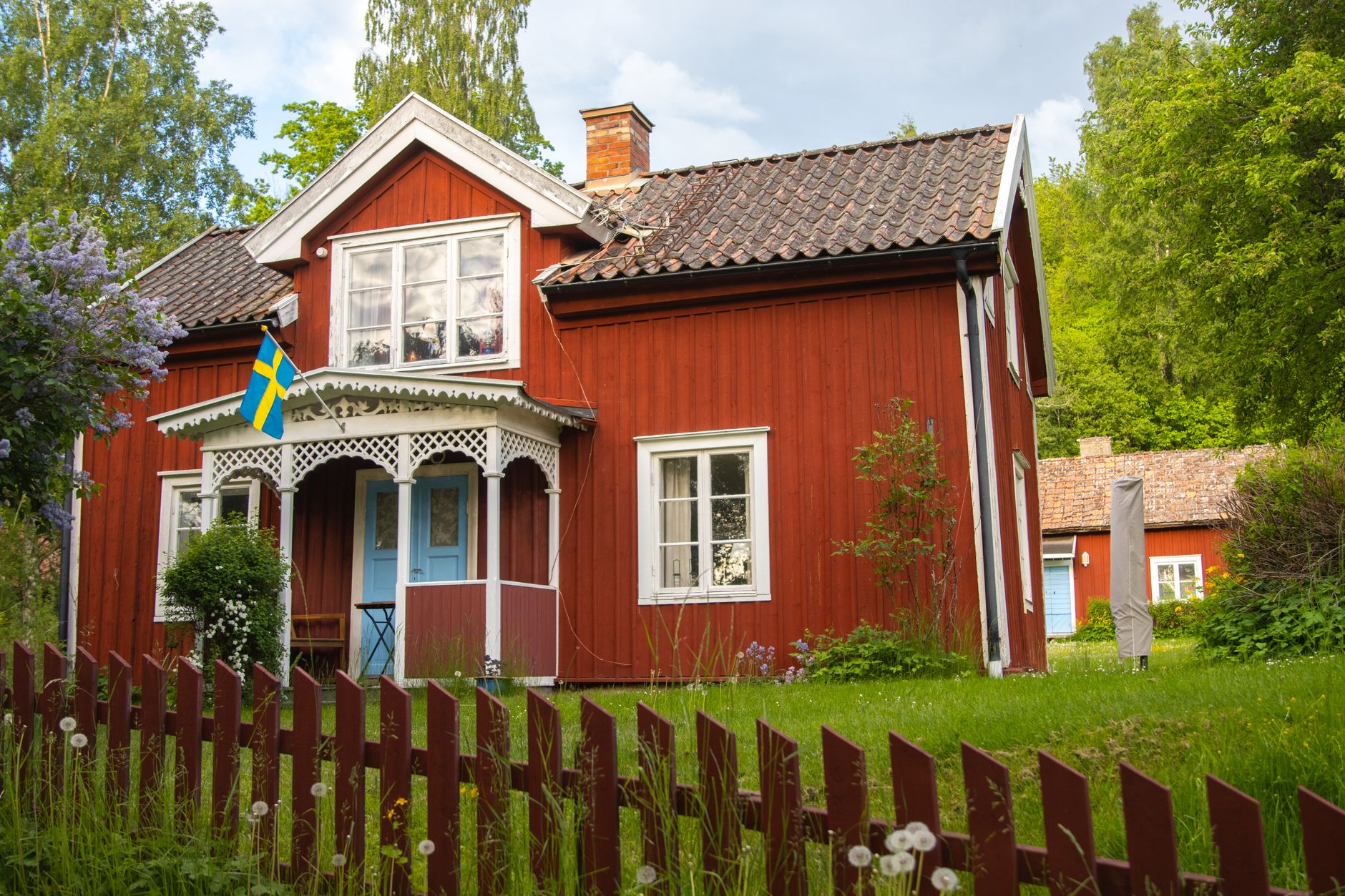 Traditional red Swedish cottage with flag in Gränna, surrounded by lush greenery.