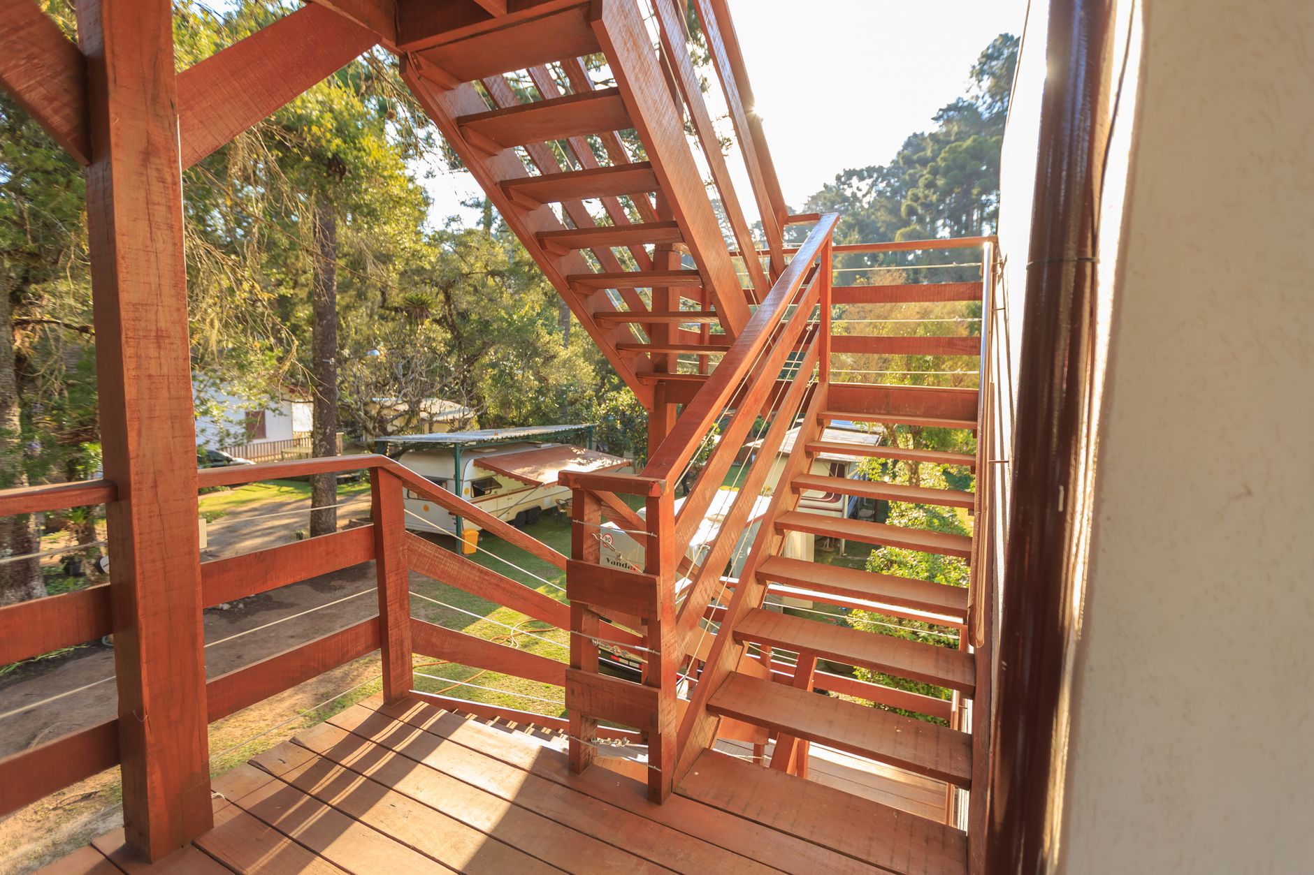 Wooden staircase basking in sunlight, surrounded by lush trees in an outdoor park setting.