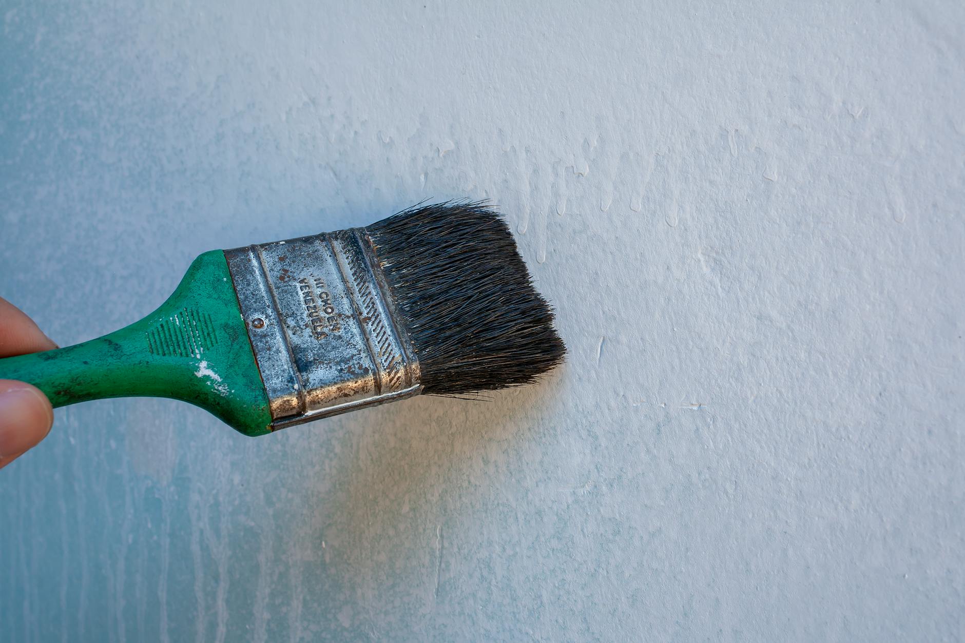 Close-up of a hand painting a wall with a paintbrush, perfect for renovation and DIY themes.