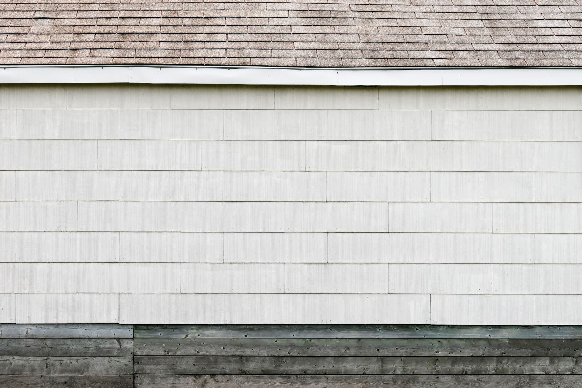 A minimalist exterior wall with white siding and a shingled roof, showcasing clean lines and simplicity.