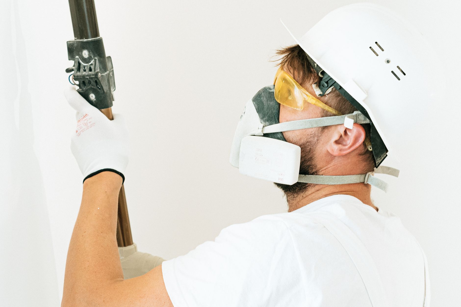 Construction worker wearing safety gear applying paint with a roller indoors. Focus on safety measures.