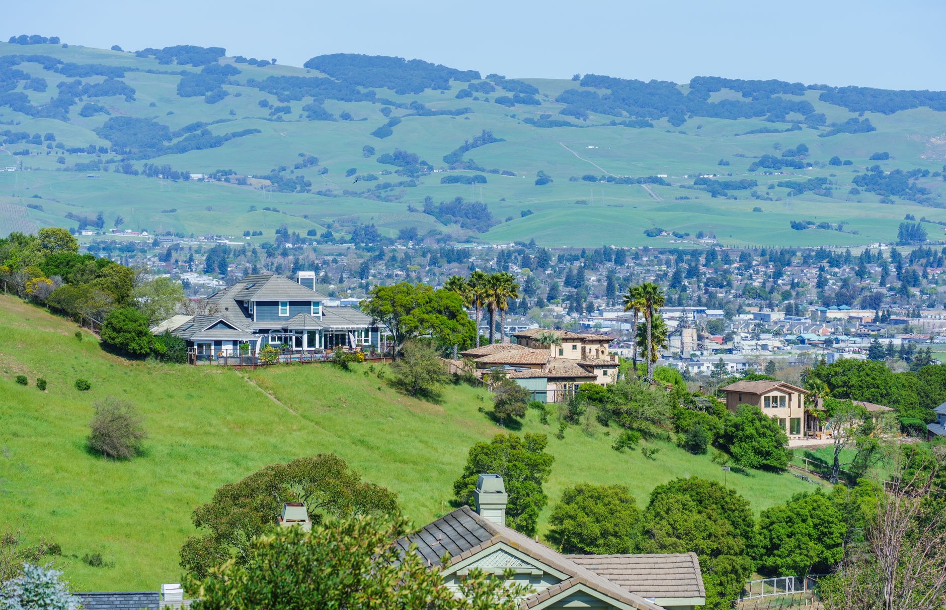 Charming hillside houses with lush green surroundings, overlooking a sprawling valley on a sunny day.
