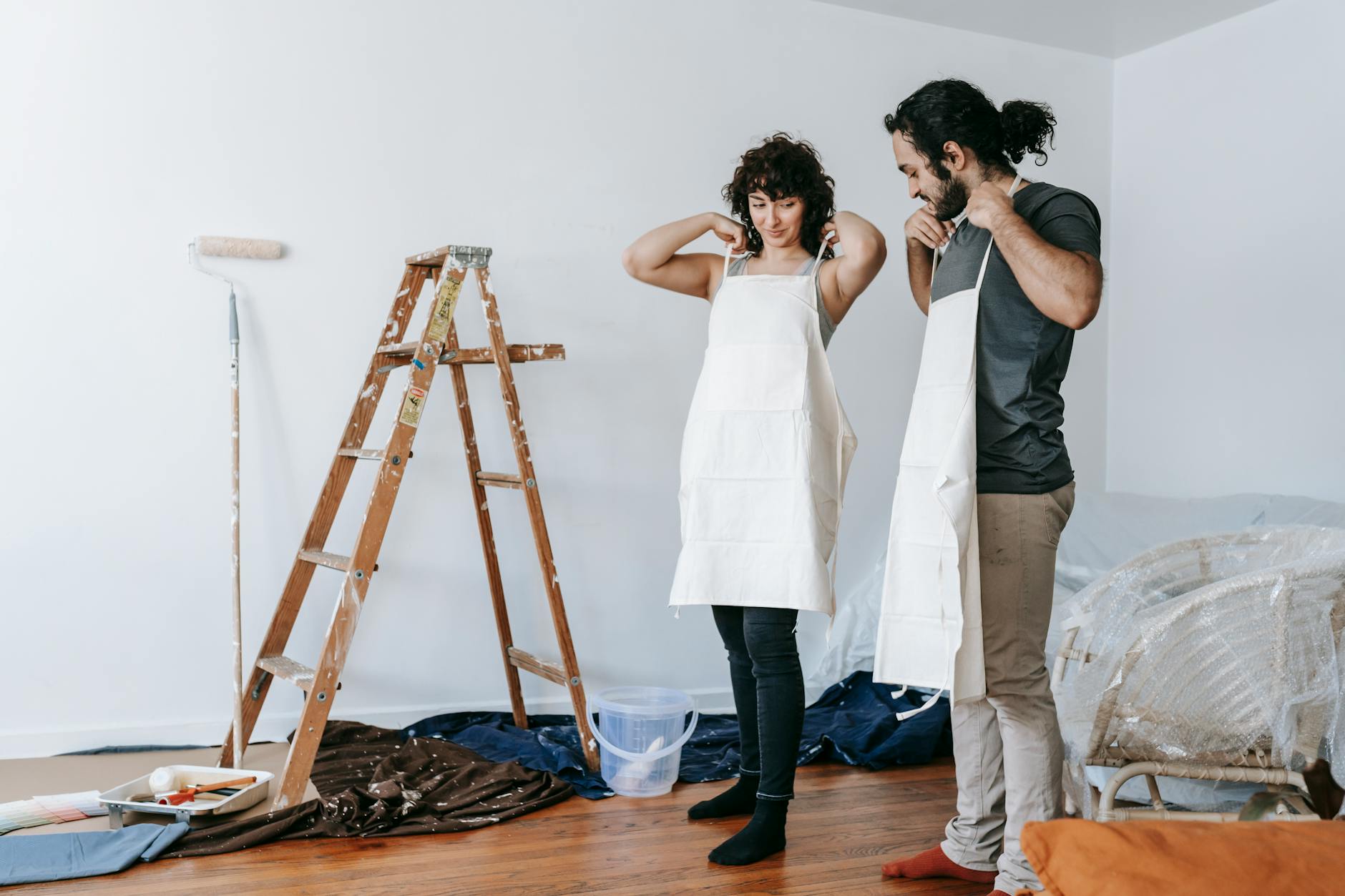 A couple prepares for home renovation, wearing aprons in an indoor setting.