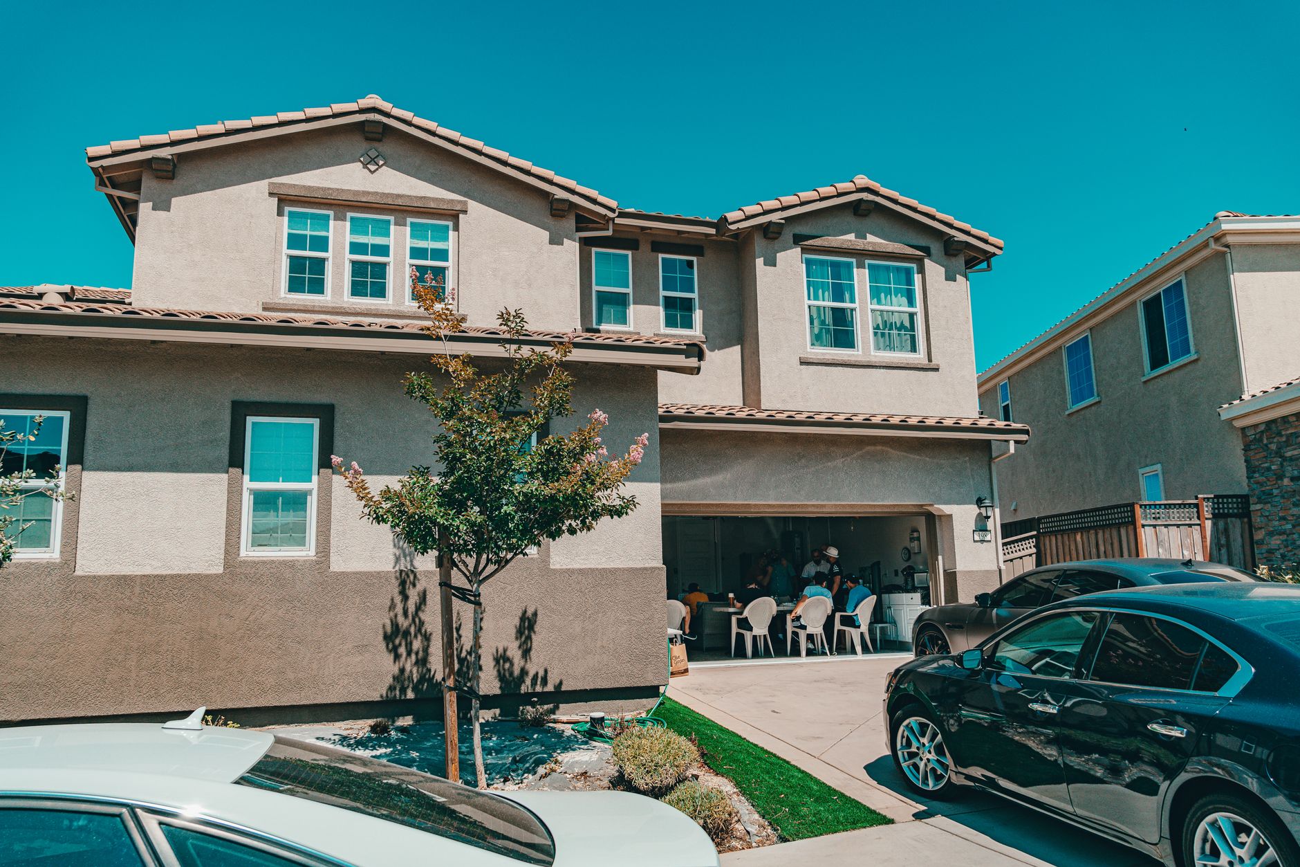 Two-story suburban house with people gathered in the garage, Hayward, CA.