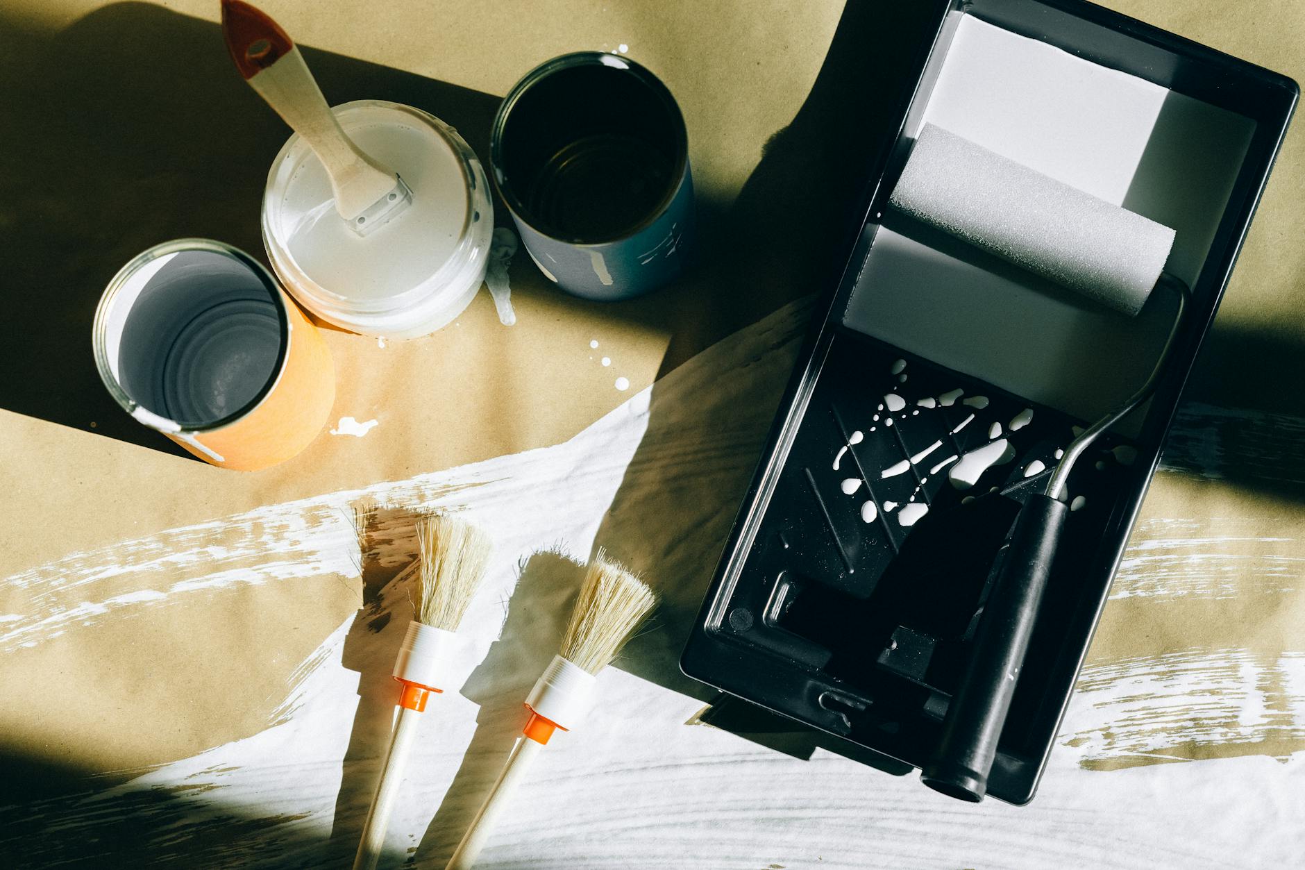 Top view of painting tools including brushes, rollers, and paint cans on paper.