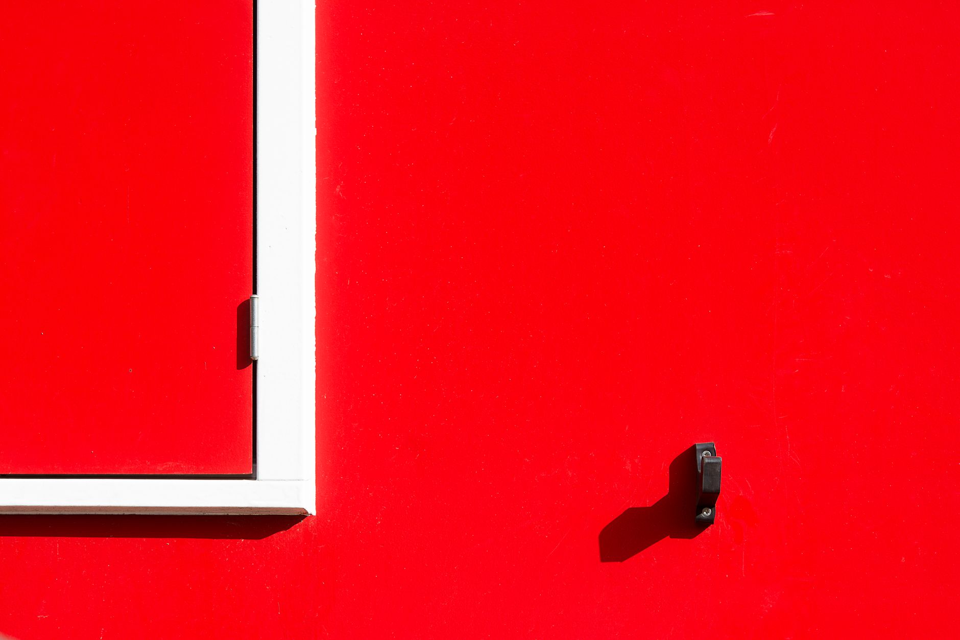 Bright red wall featuring a white door frame and shadow in a minimalist style.