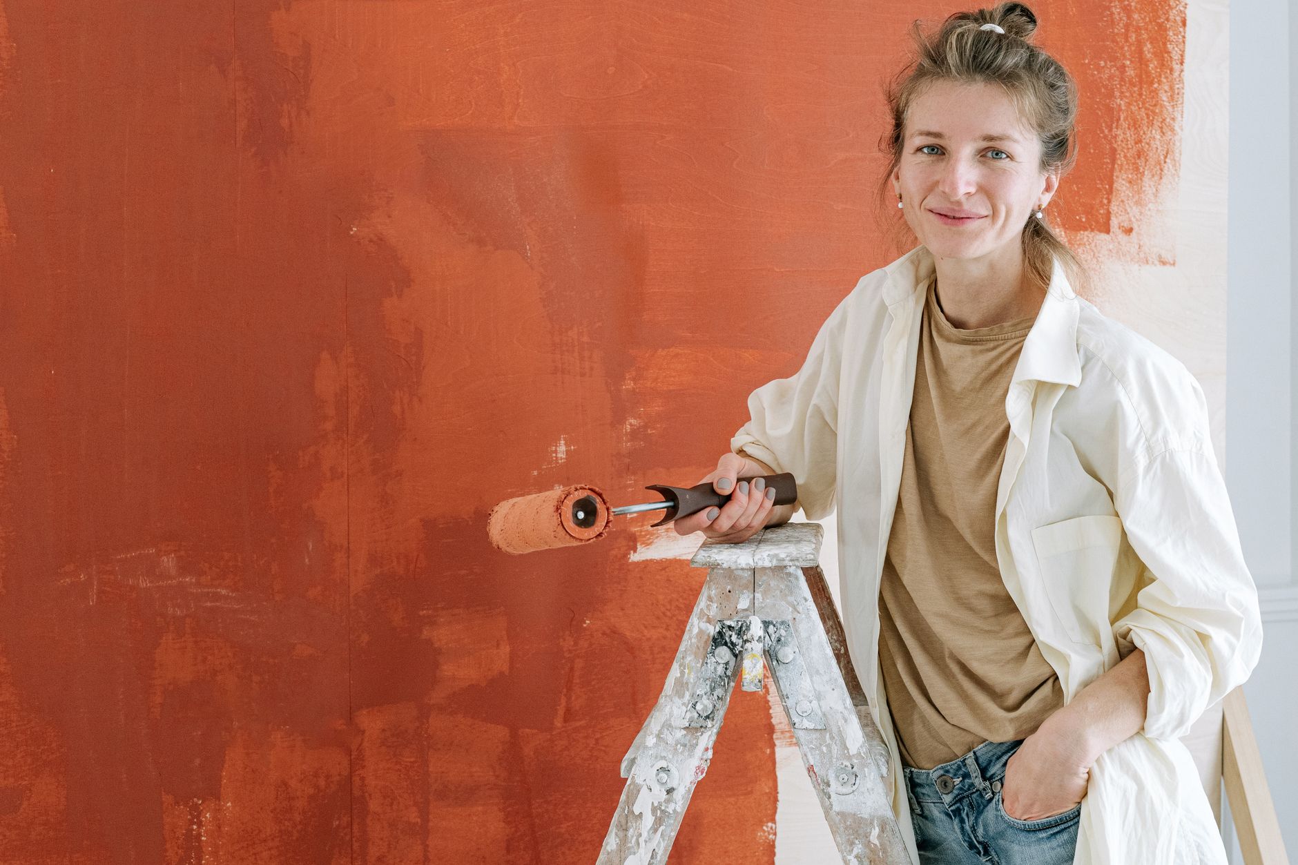 Woman smiling while painting a wall with a roller during a home renovation project.