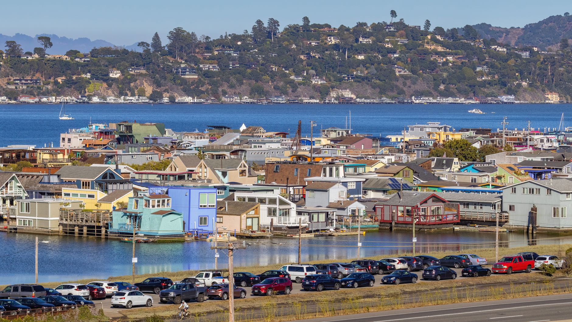 Scenic view of colorful waterfront homes with cars parked in the foreground and mountains in the background.