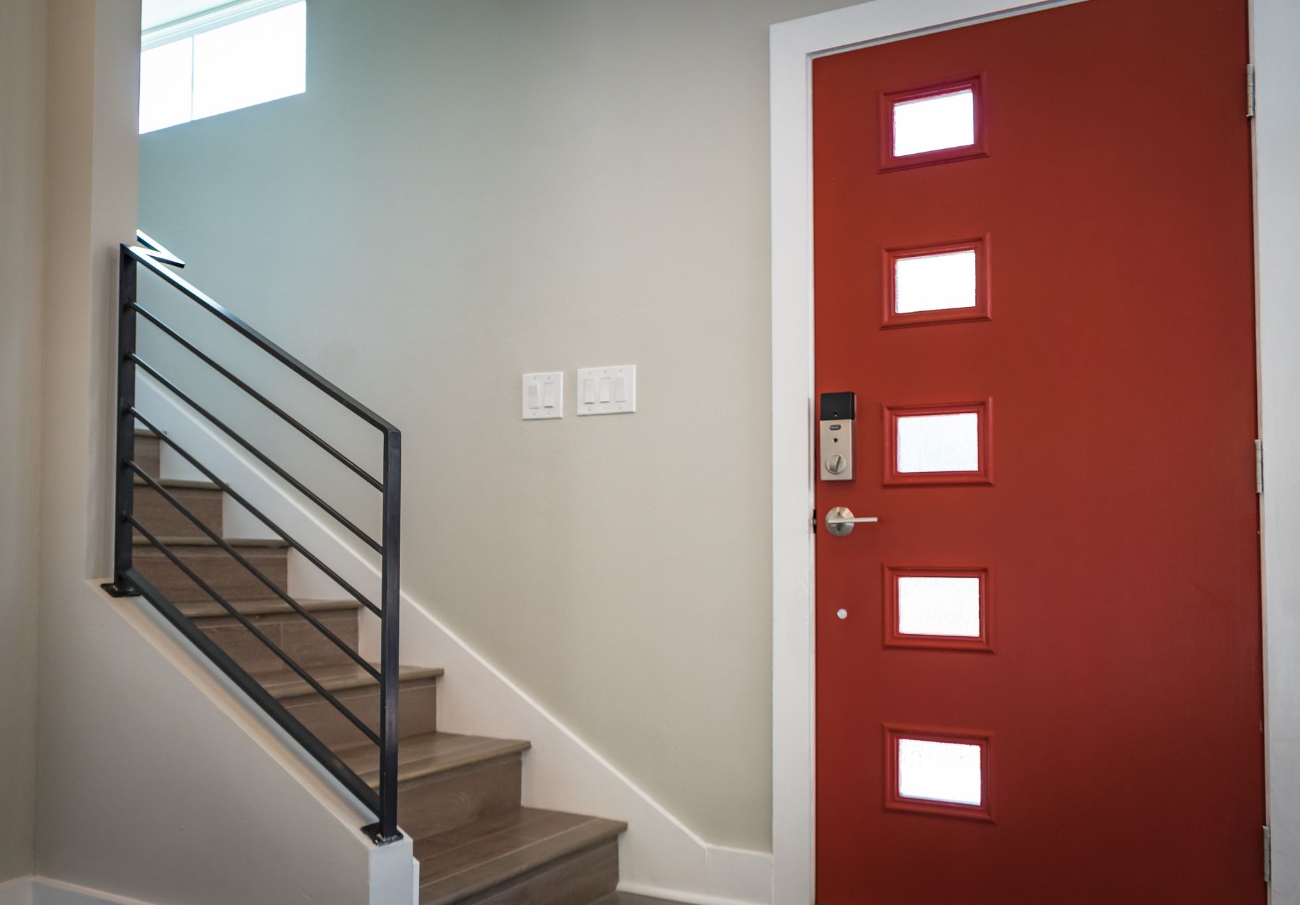 Contemporary interior with a vibrant red entrance door and stairs, showcasing minimalist design.