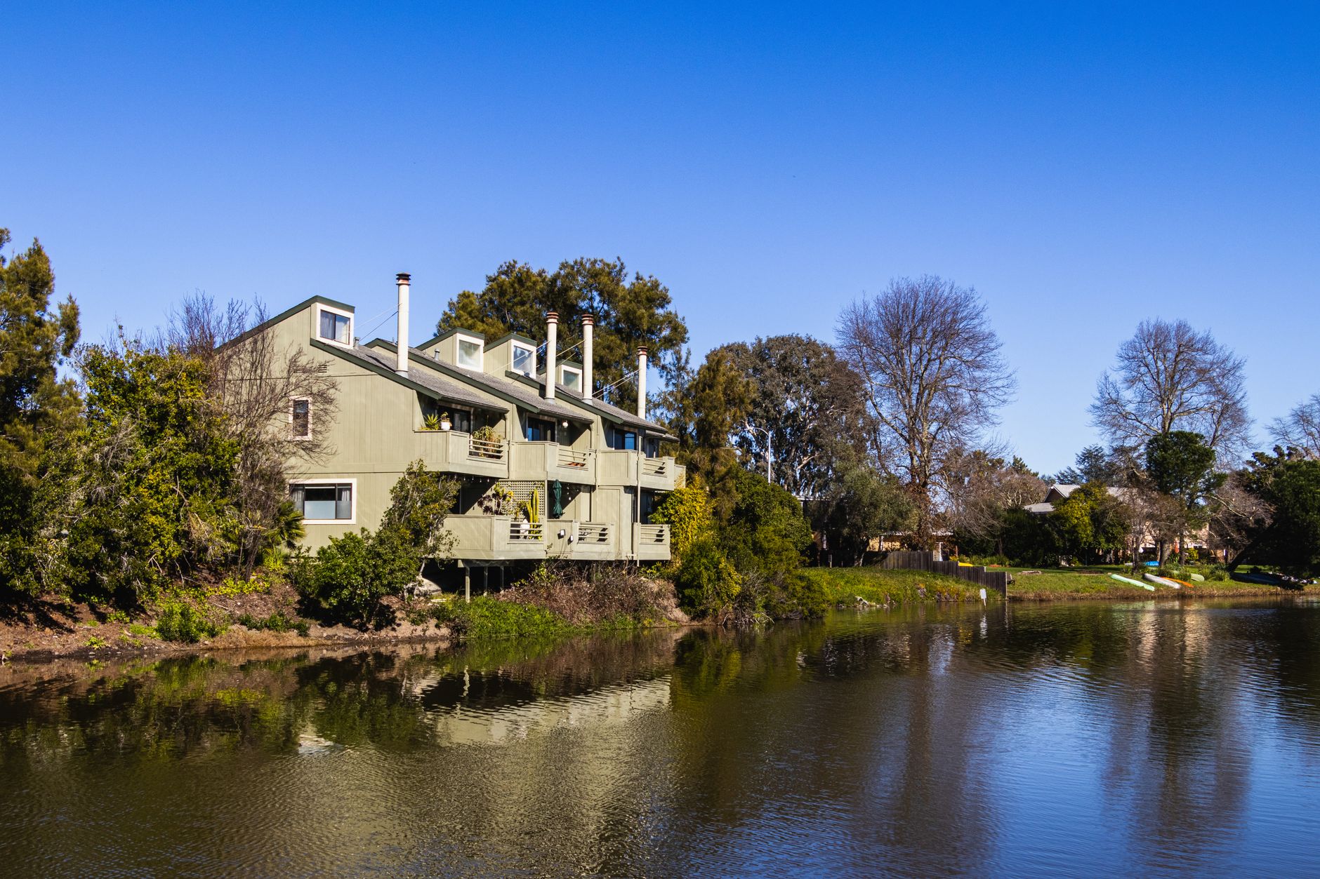 A contemporary residential building with balconies next to a serene river surrounded by trees.
