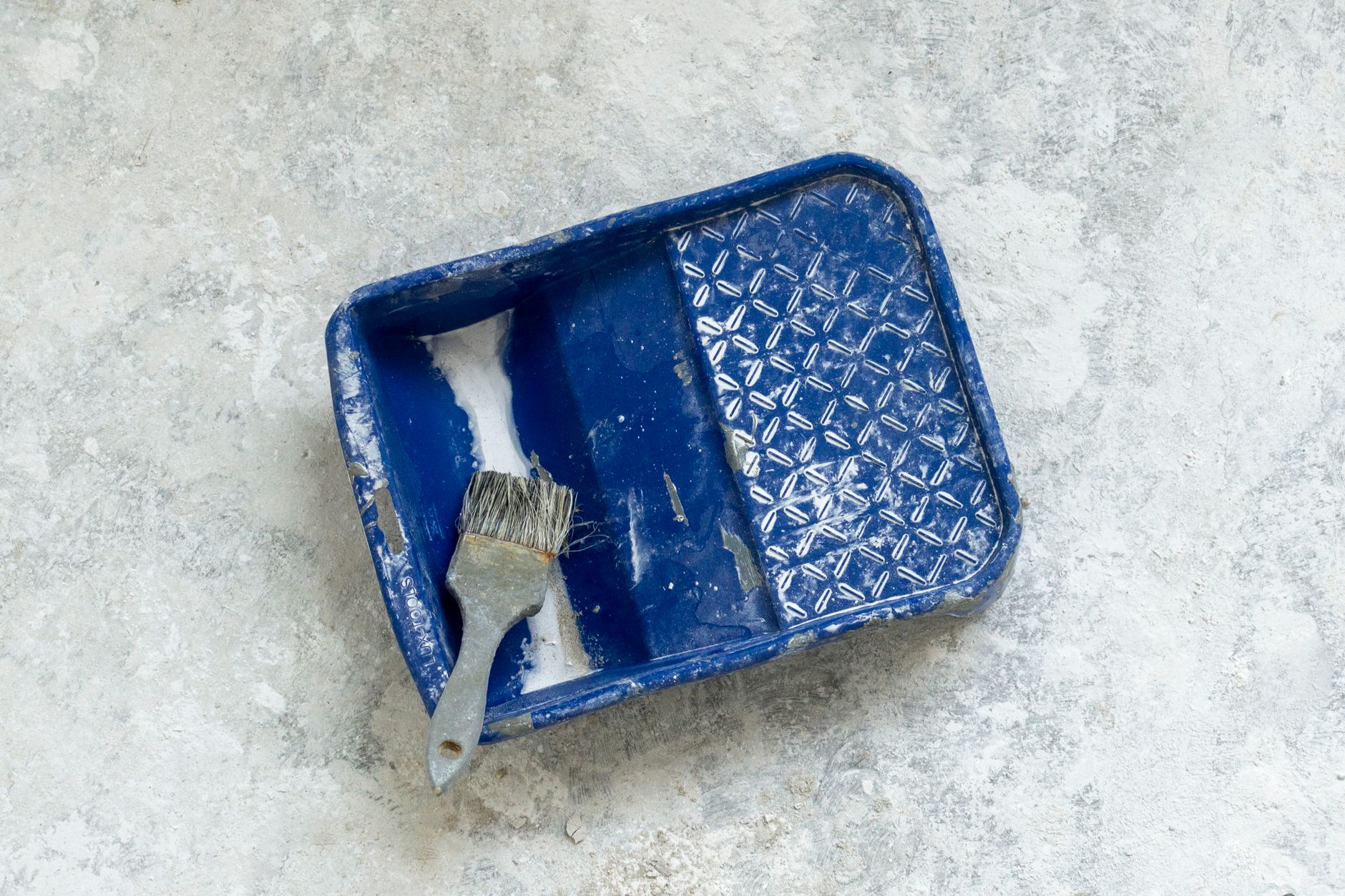 Stock photo of a well-used blue paint tray and brush on a textured surface, perfect for renovation themes.