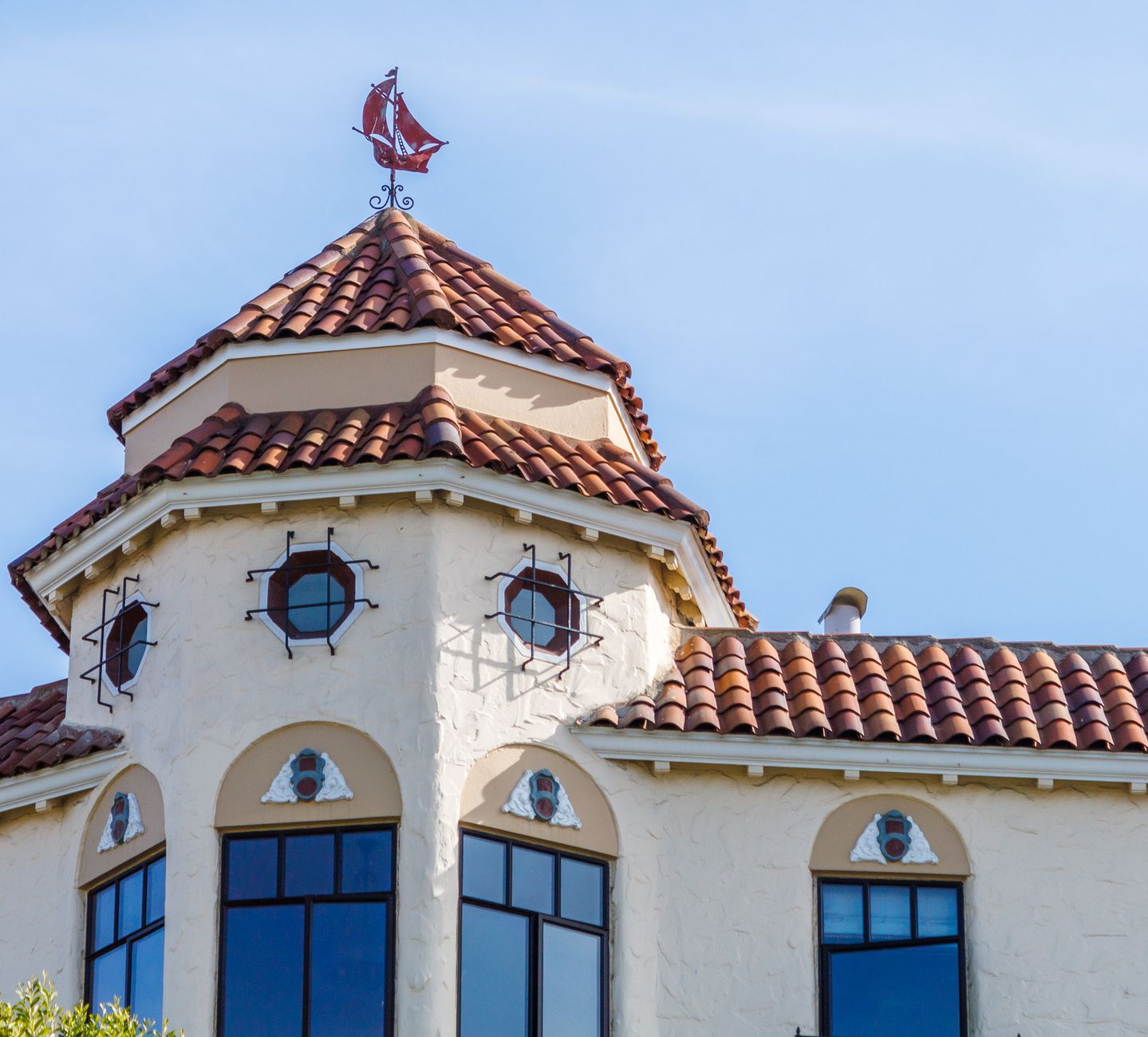 A picturesque building with terracotta-tiled roof and unique ship weather vane, reflecting classic Mediterranean architecture.