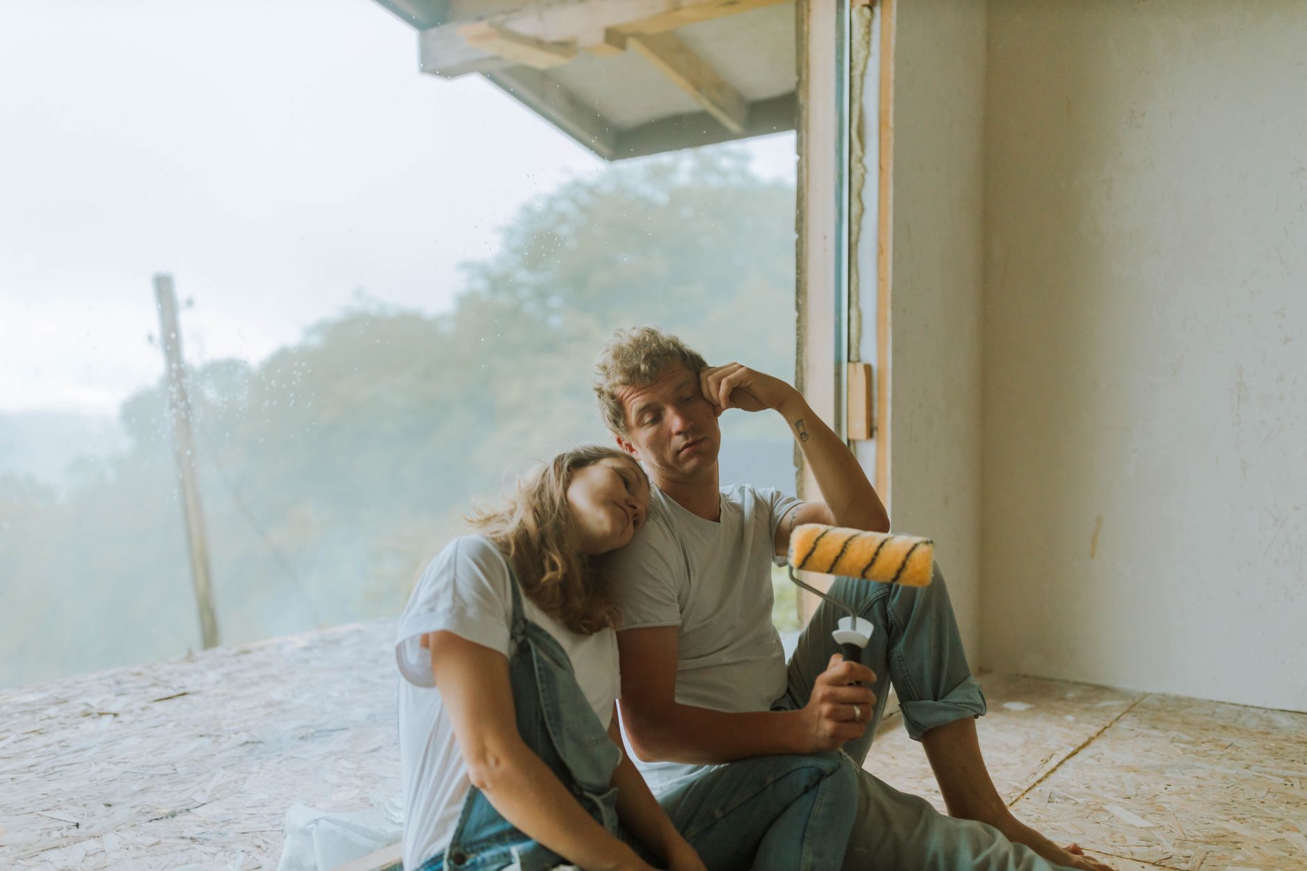 A couple taking a break while renovating their home, sitting indoors with a paint roller.