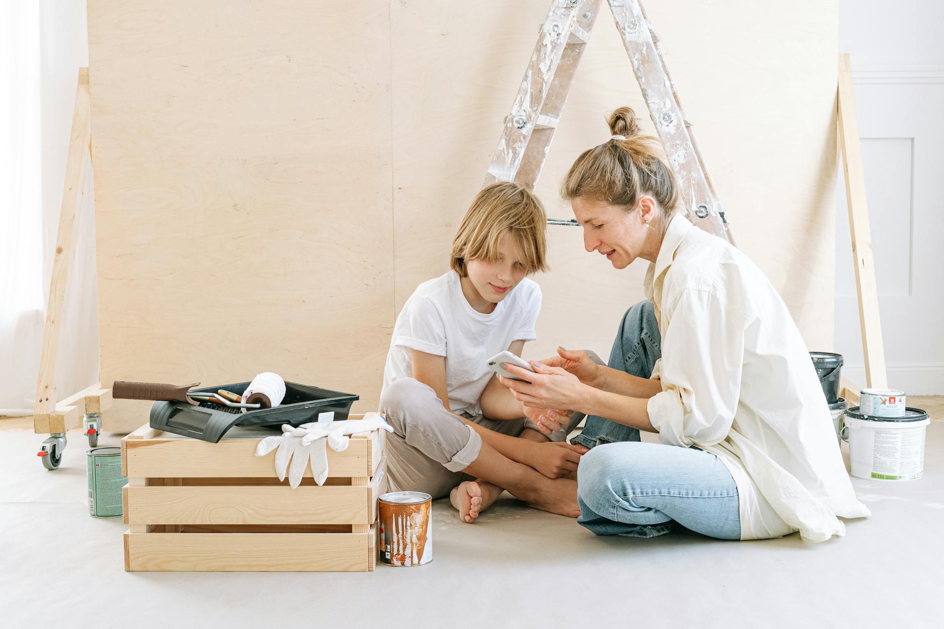 Mother and son working on a room renovation project, seated on floor with painting supplies.