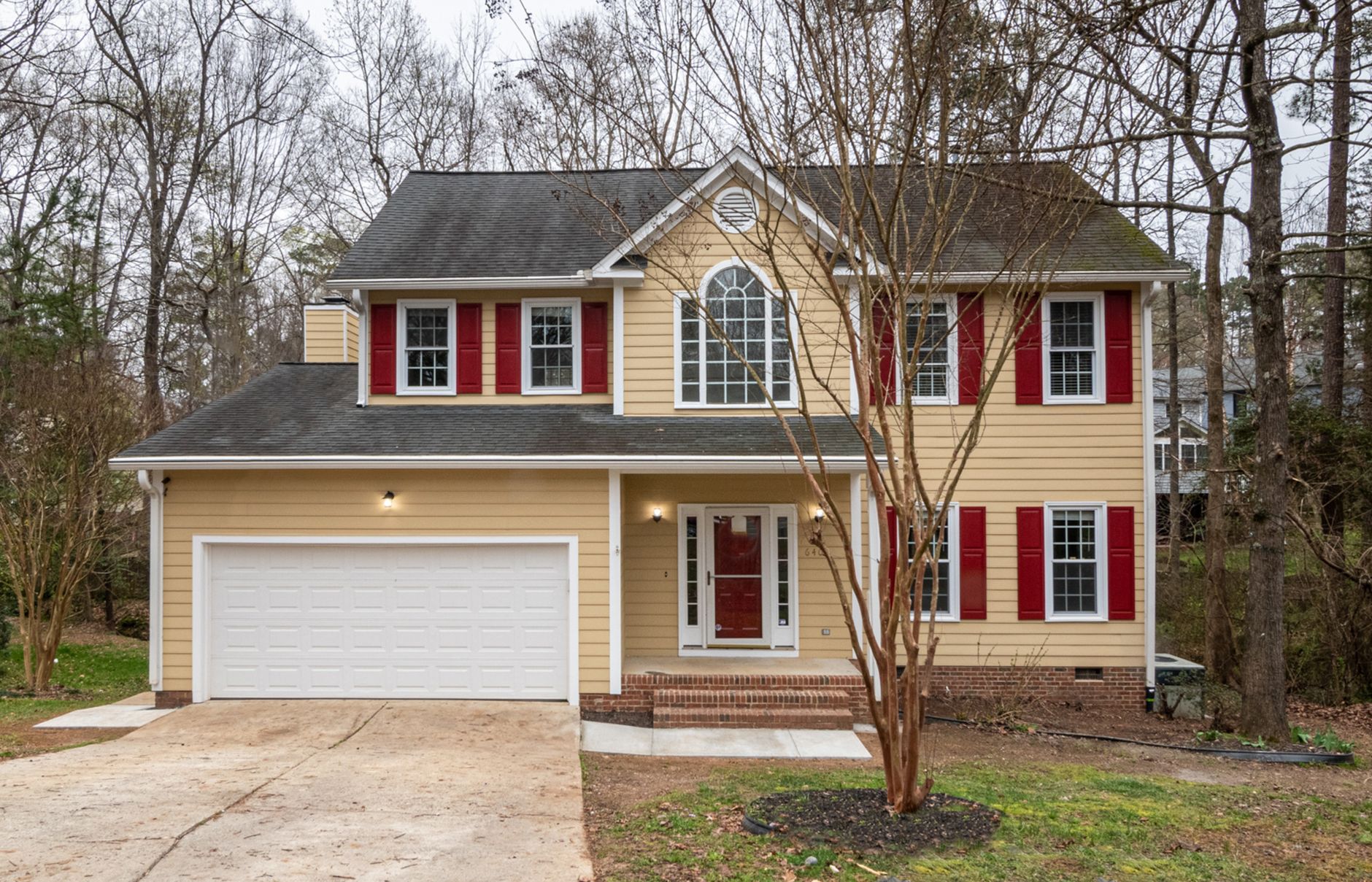 A picturesque suburban home featuring red shutters and surrounded by greenery.
