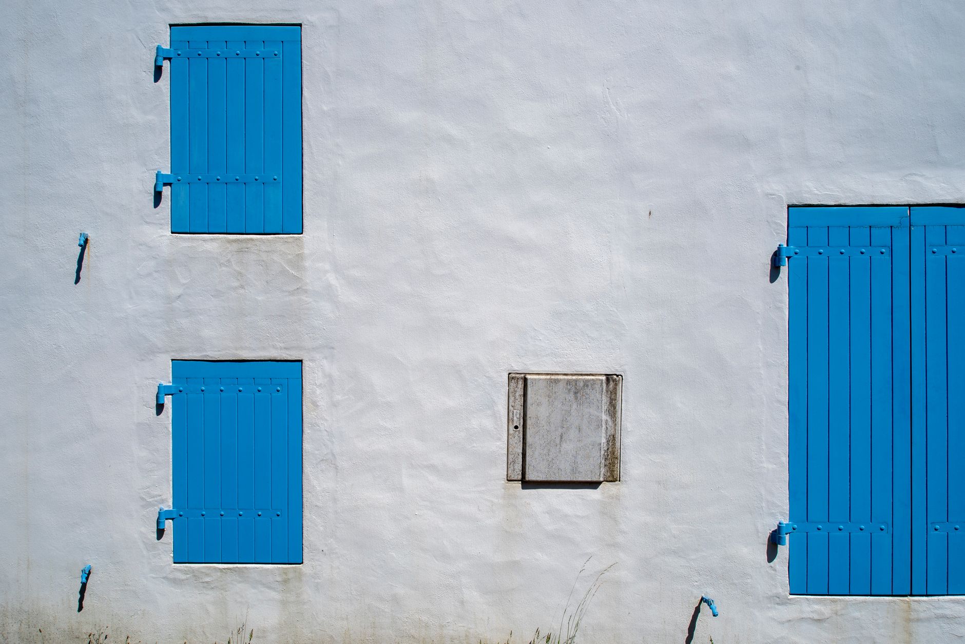 Minimalist architecture with blue shutters on a white wall, creating a vivid contrast.
