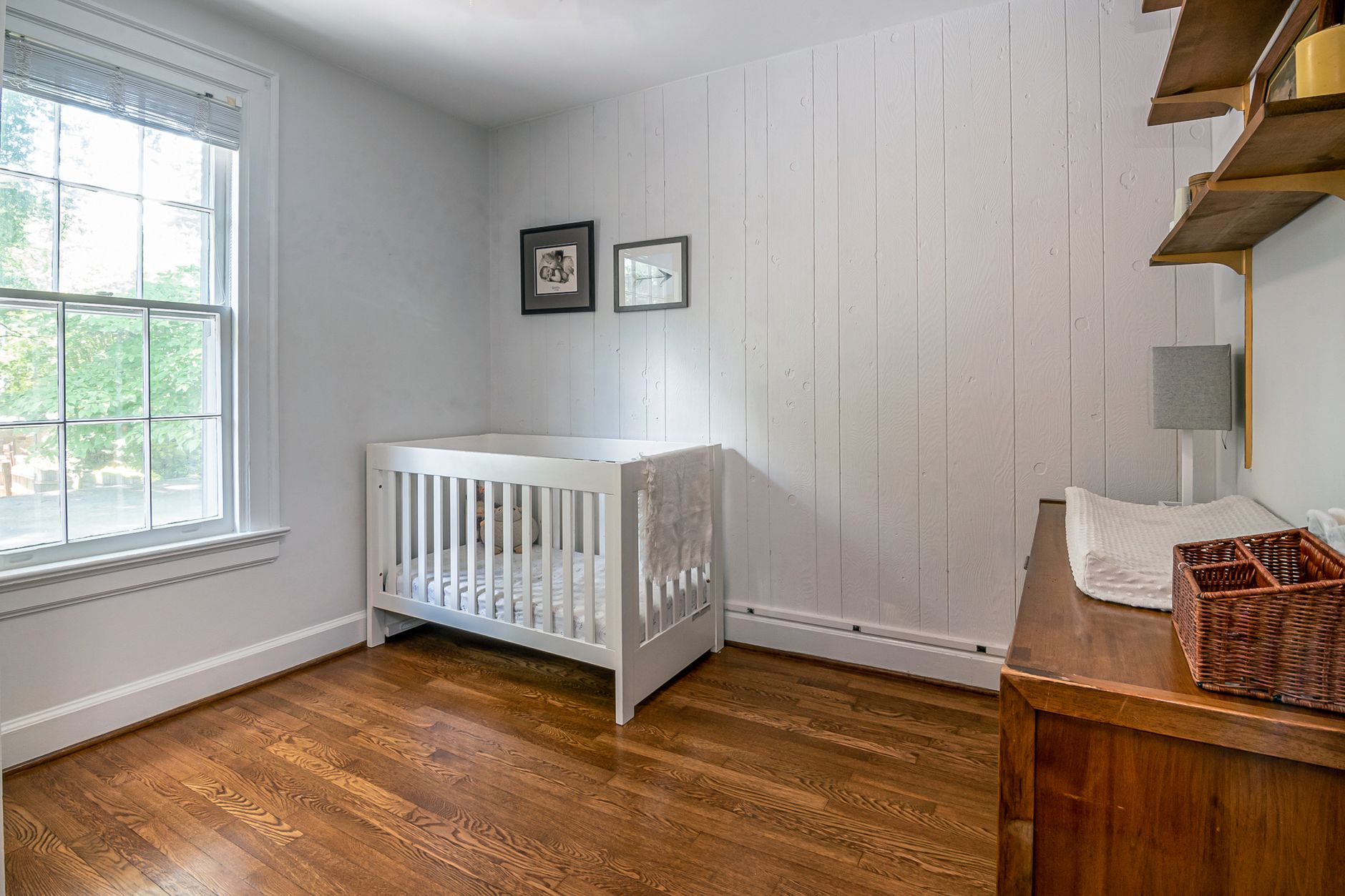 Serene baby room with crib, wooden flooring, and bright window light.