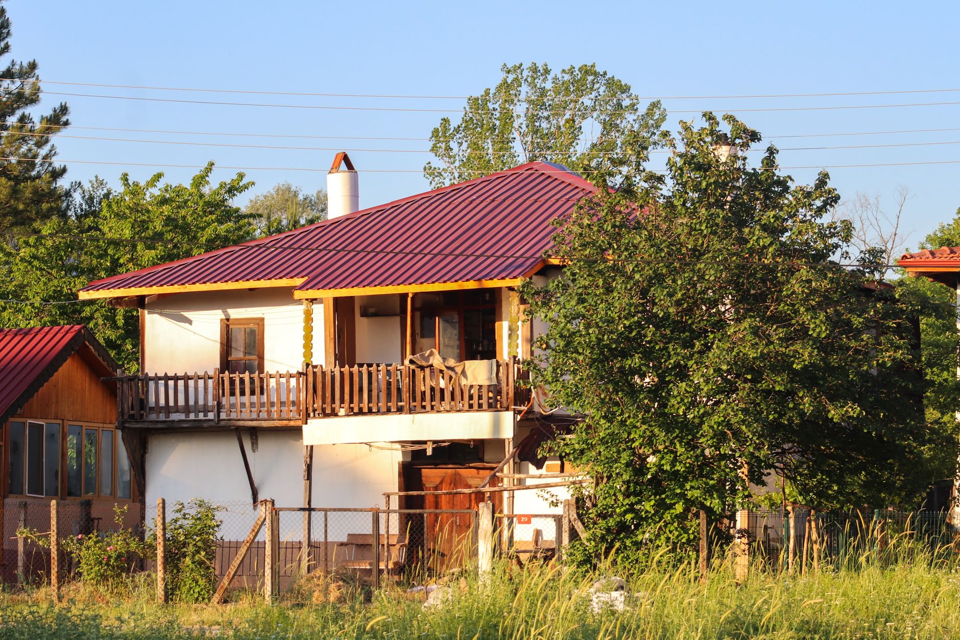 Rustic home with a vibrant red roof and lush surroundings under a clear sky.