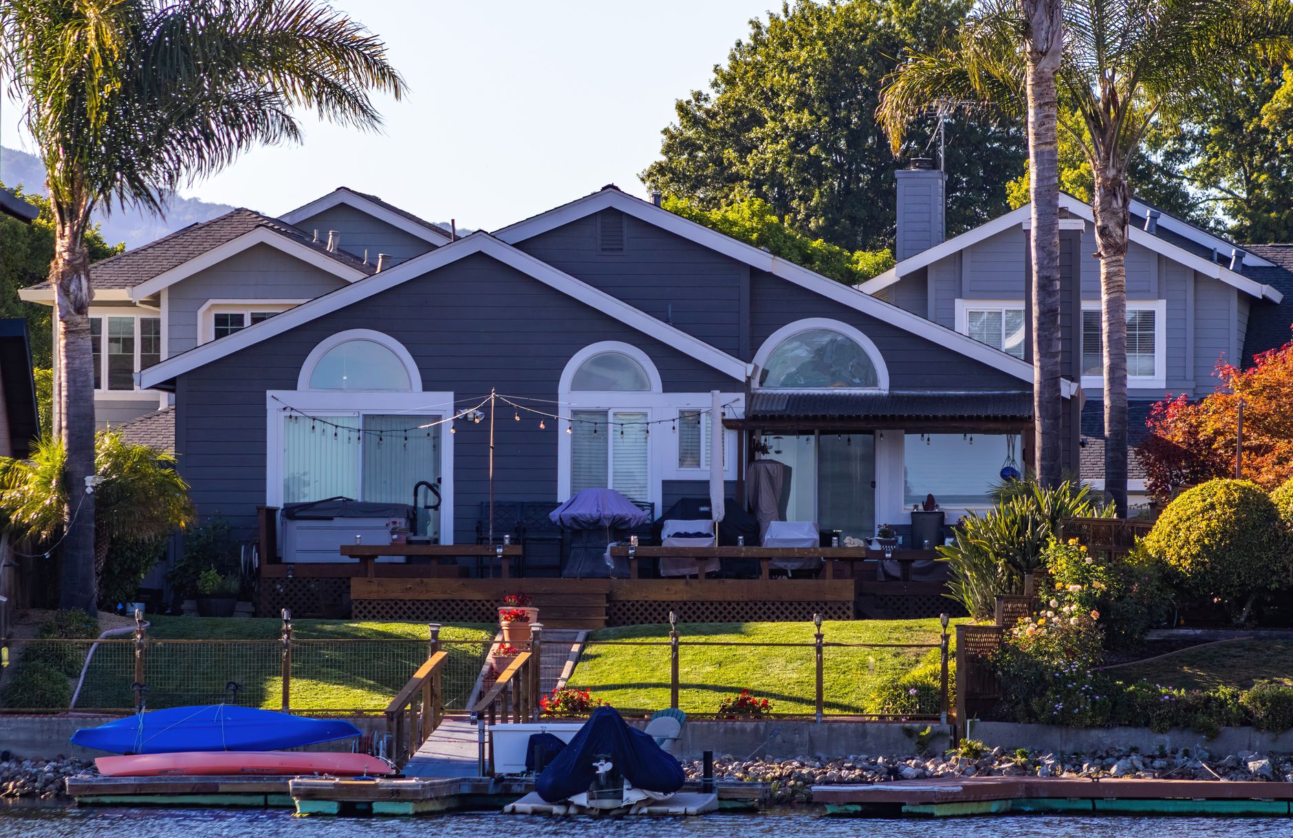 A picturesque seaside home featuring a cozy patio, lush garden, and palm trees by the ocean.