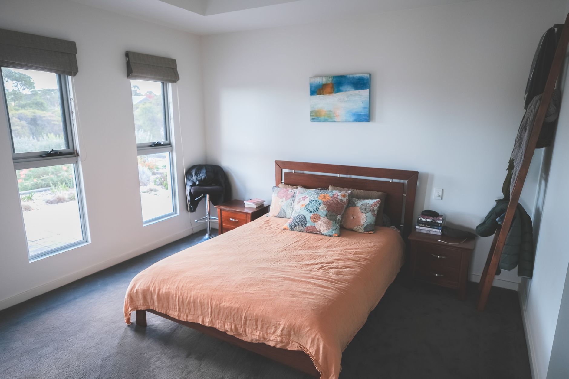 Interior of light bedroom with simple wooden furniture and cozy bed with decorative cushions in daytime