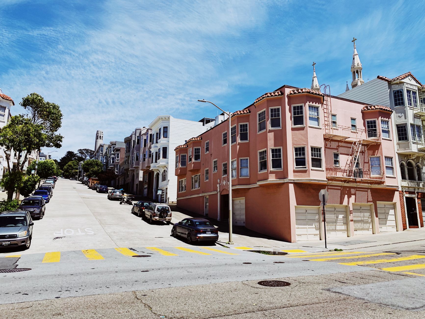 Charming residential street with colorful buildings, parked cars, and blue sky in San Francisco.