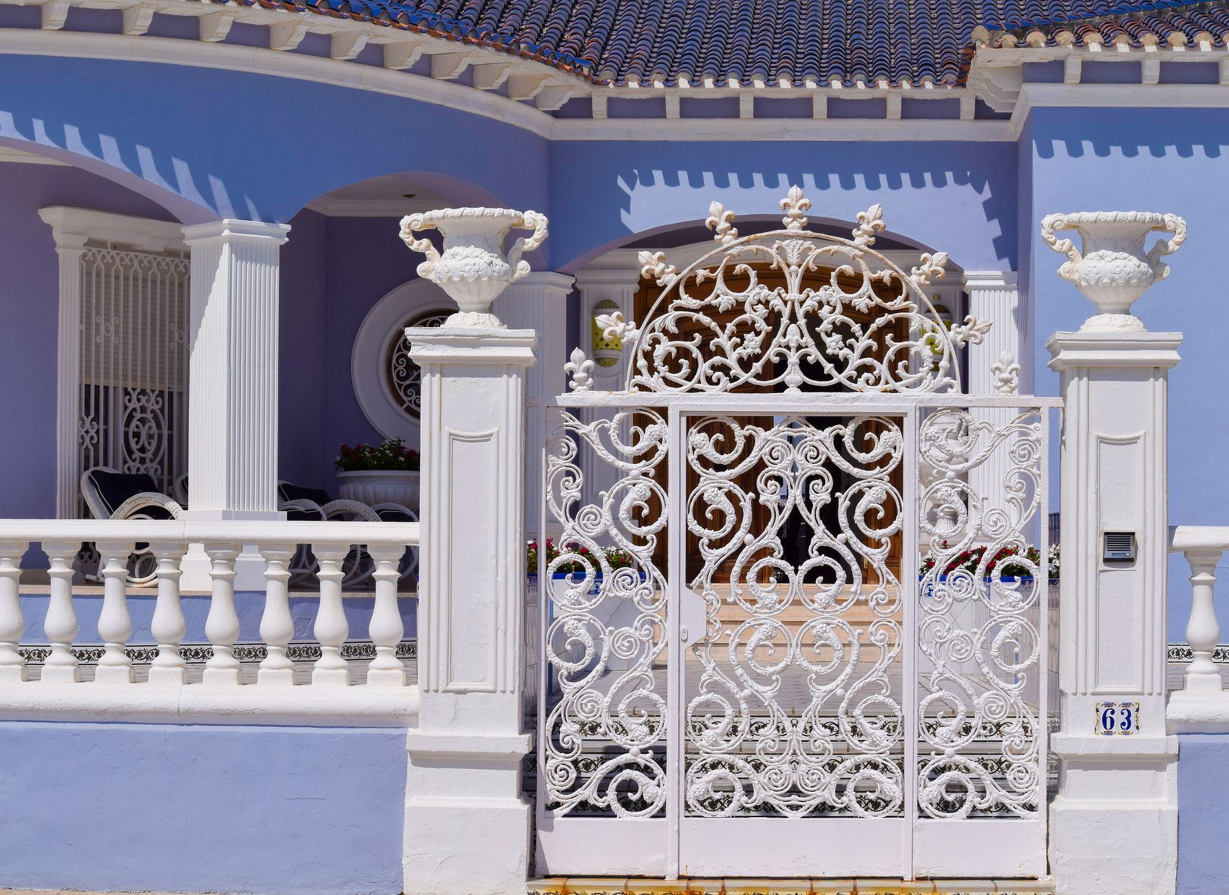 Ornate white iron gate and columns in front of a blue villa in Torrevieja, Spain.