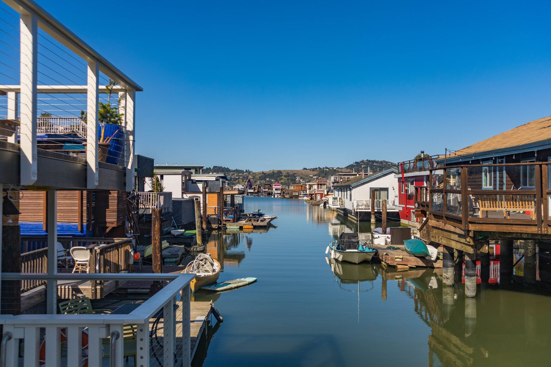 Peaceful canal with floating houses and boats under clear sky.