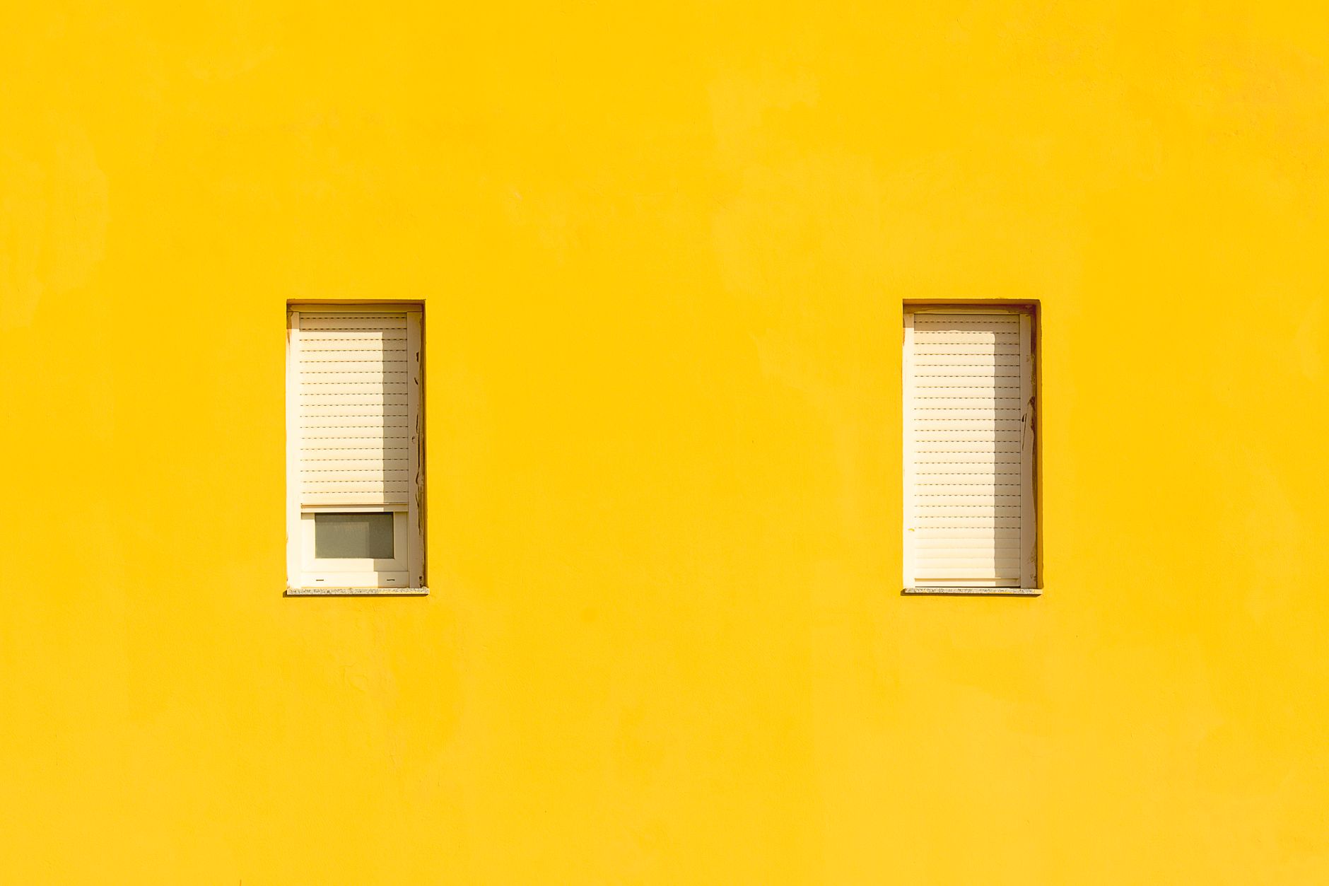 Bright yellow wall with two shuttered windows, creating a minimalist and modern aesthetic.