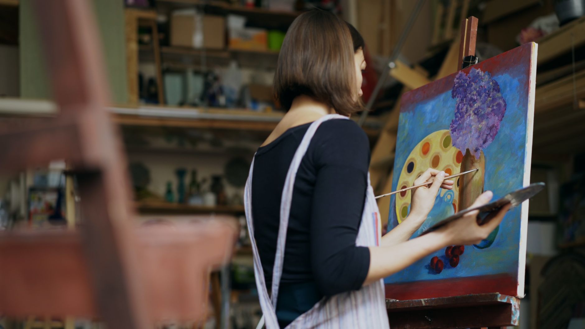 A woman artist painting on a canvas in her art studio, creating a colorful piece.