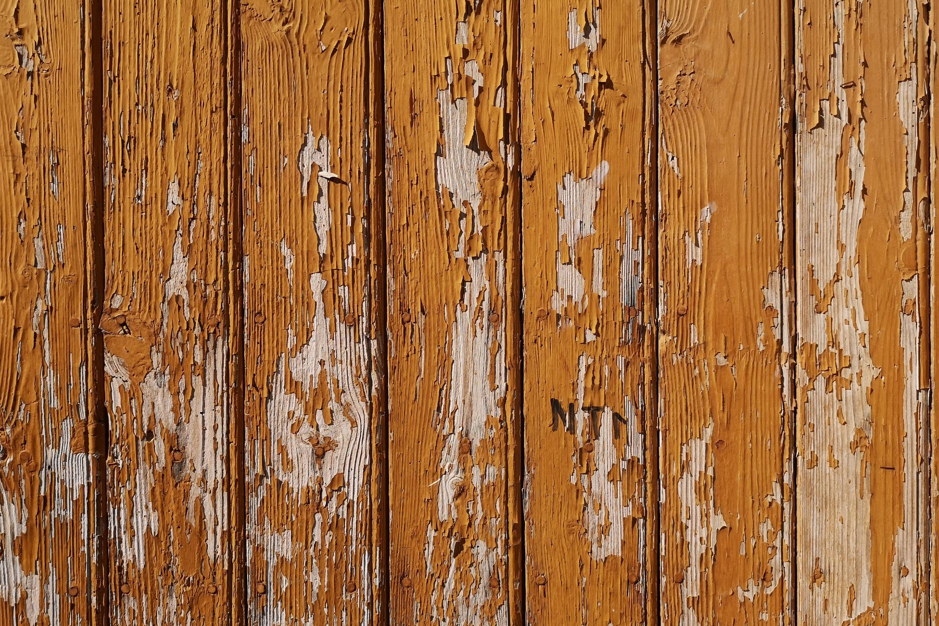 Close-up of aged wooden planks with peeling brown paint, showcasing rustic texture and weathered appearance.