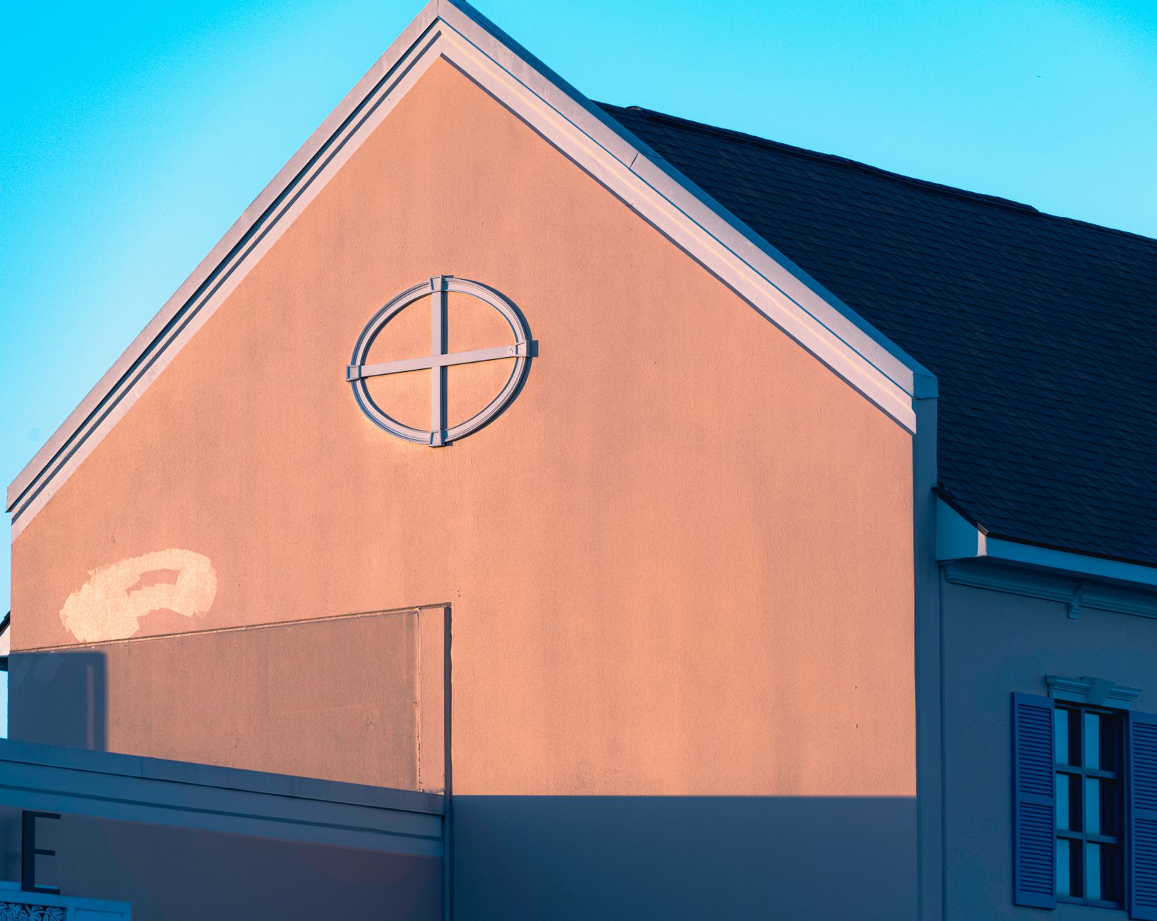A minimalist photo of a pink building wall with a sun cross window, captured in urban sunlight.