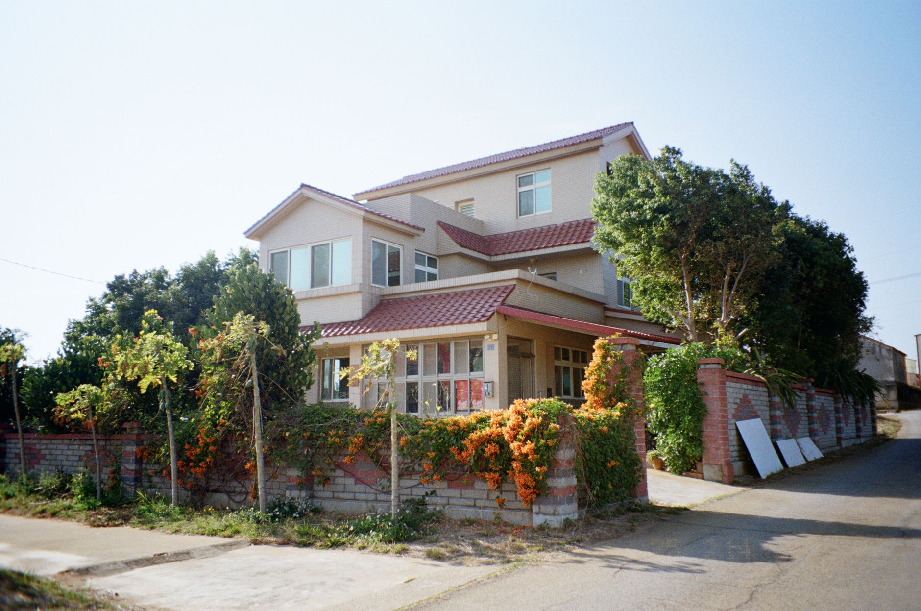 A charming suburban house with a red roof, surrounded by lush greenery and a garden, basking in daylight.
