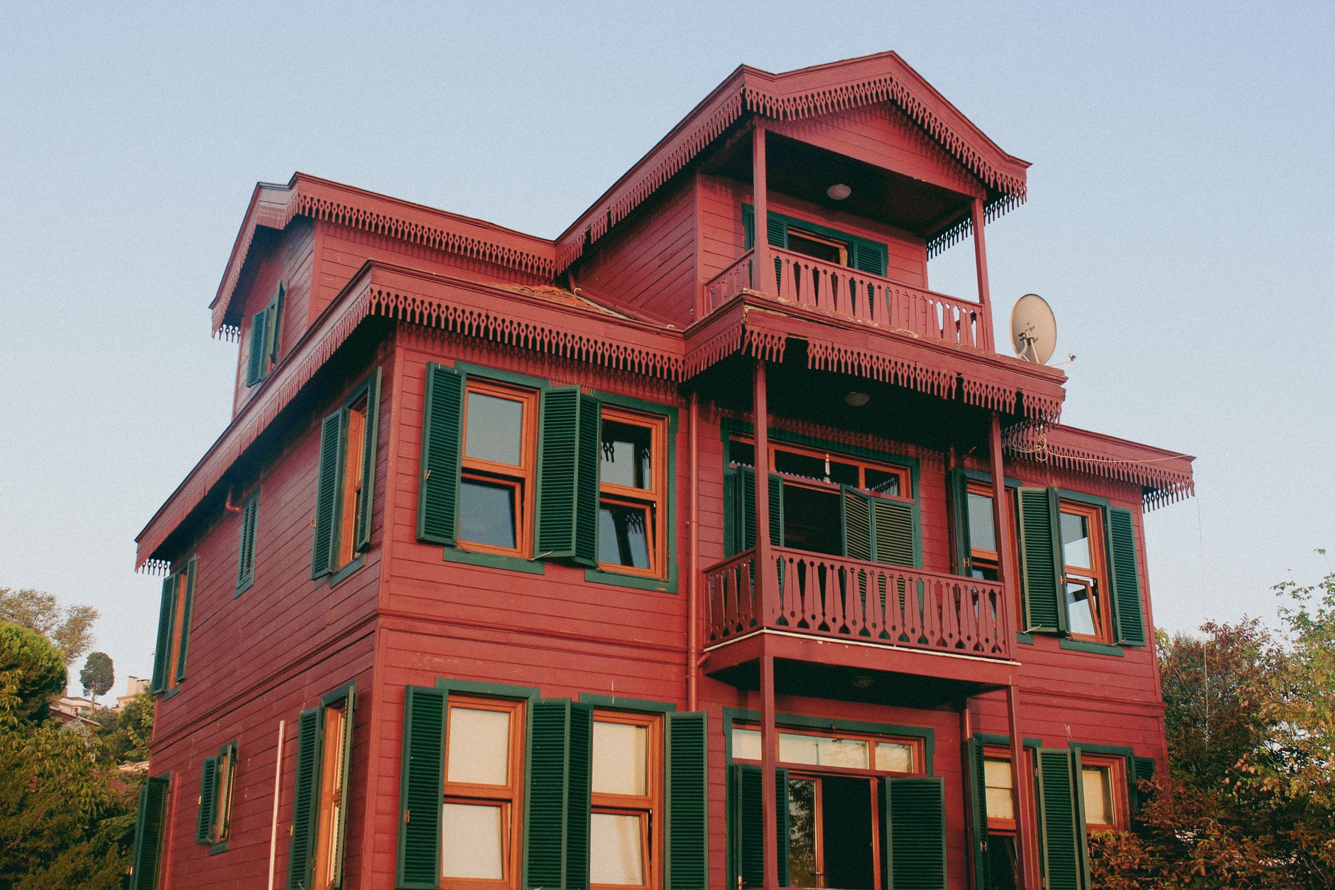 A charming three-story red wooden house with green shutters and intricate trim, photographed from a low angle.