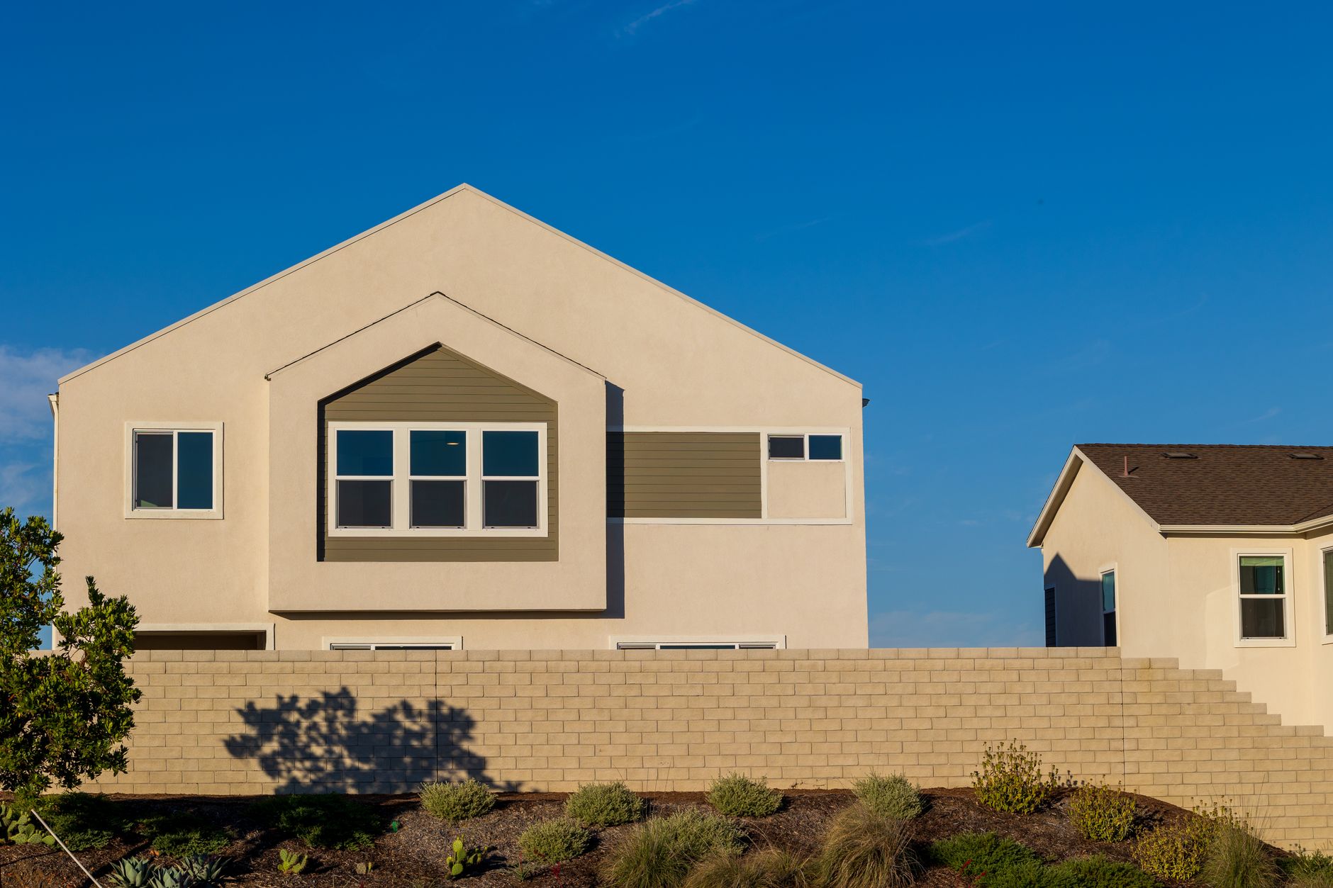 A modern suburban house with a sunlit facade against a clear blue sky.